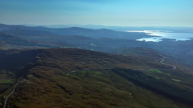 Caha Pass, County Cork, Ireland, September 2024. Drone ascends and orbits clockwise high above mountain road with grand scenic vistas south east to Glengarriff and the glistening North Atlantic Ocean.
