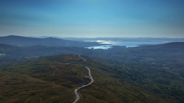 Caha Pass, County Cork, Ireland, September 2024. Drone panoramic aerial pullback above winding road following the ridge down towards Glengarriff and the North Atlantic Ocean.