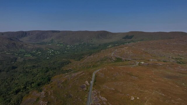 Caha Pass, County Cork, Ireland, September 2024. Drone ascends and pushes forward above the winding road above the mountainous landscape as cars navigate scenic views on the border with County Kerry.