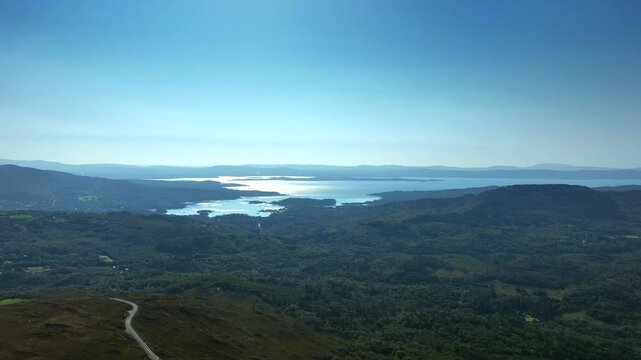 Caha Pass, County Cork, Ireland, September 2024. Drone descends facing south east towards Glengarriff with the North Atlantic Ocean in the distance as the mountains slopes down with winding road.
