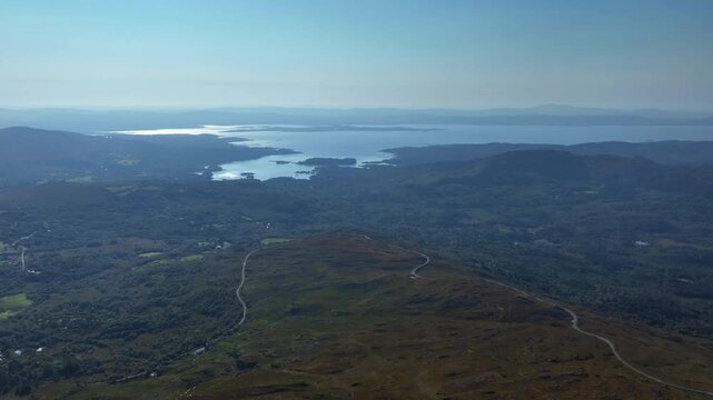 Caha Pass, County Cork, Ireland, September 2024. Drone orbits counter clockwise and pulls backward high above a winding mountain road with Gortnakilla and North Atlantic Ocean in the distance.