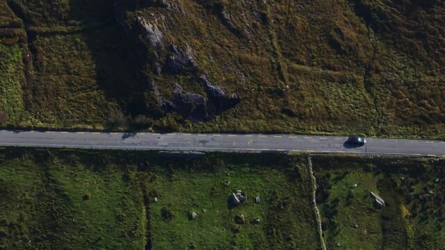 Caha Pass, County Cork, Ireland, September 2024. Drone in Bird's Eye view follows car as it navigates the twisting mountain road between grassy slopes near the border with County Kerry.