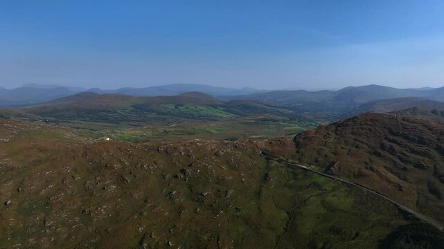 Caha Pass, County Cork, Ireland, September 2024. Drone ascends above a winding road via Turners Rock Tunnel into County Kerry through the grassy rugged mountain slopes.