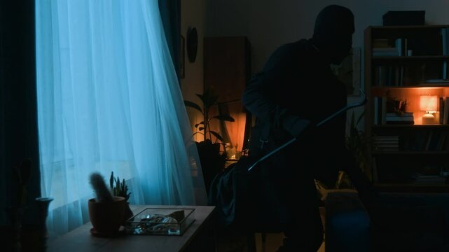 Two criminals dressed in black clothes coming down from windowsill after breaking into property through window