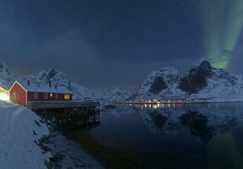 Fototapeta premium A winter landscape with aurora borealis, at night, on the Lofoten Islands in Norway. Green northern lights above mountains in the evening. Polar lights in the sky at night. A polar night landscape