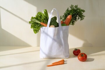 White reusable bag filled with fresh vegetables and bread against a soft cream background with natural light and soft shadows for a clean, vibrant look