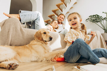 Smiling, little girl sitting on the floor at home in living room, drawing and playing with dog © Maria Vitkovska