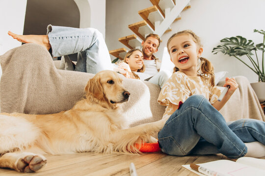 Smiling, little girl sitting on the floor at home in living room, drawing and playing with dog
