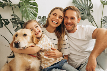 Happy mother, father, cute, little daughter hugging together with dog, golden retriever