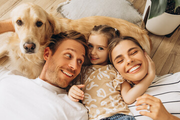 Smiling family and golden retriever hugging together, lying, embracing in cozy living room at home