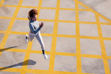 from above of determined female jogger in sportswear running on pavement with ornament and shadow in sunlight, concept of urban sport and healthy lifestyle, copy space for text