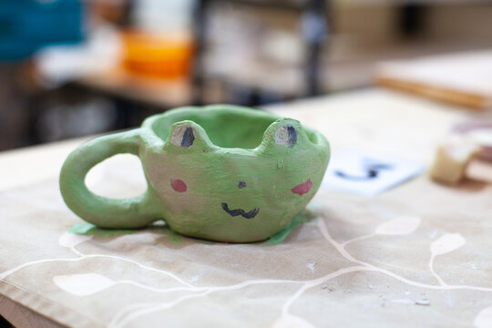 Cute frog cup made from clay by child. Children's workshop at pottery studio. Creating ceramics with own hands.