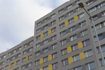 The apartment building features a gray exterior with yellow accents under a dramatic, cloudy sky