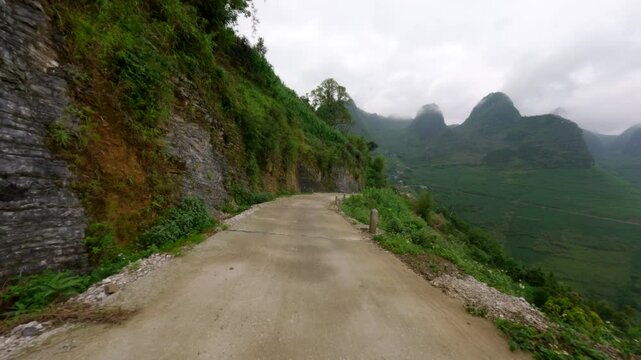 POV view from a scooter along Ha Giang Loop, showing rugged countryside and winding roads rounding bend descending on dirt