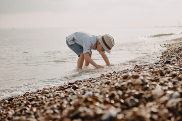 little boy wearing hat and glasses plays in the sea 