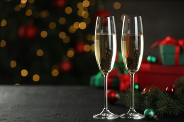 Champagne in glasses and decor on black table against blurred Christmas lights, space for text