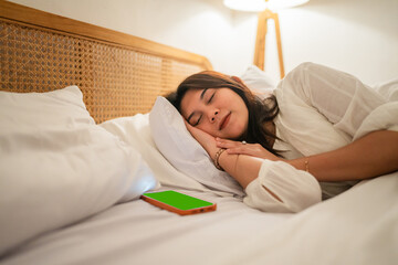 A peaceful moment of a woman resting in bed, with her smartphone conveniently beside her