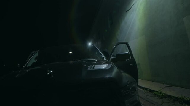 Two unrecognizable criminals running towards black car with stolen money in bag after nighttime bank robbery