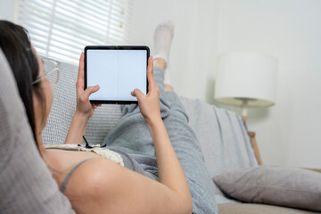 Young woman relaxing on couch using digital tablet with blank screen