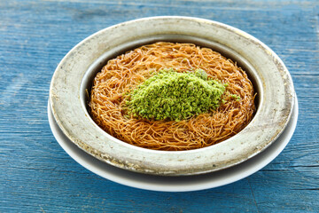 Arabic Kunafa or Baklava topped with chopped pistachio served in plate isolated on sky wooden table side view of arabic and turkish dessert