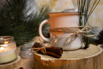 Cozy cinnamon sticks and Christmas decorated tea mug on a wood platform Candle and pine branches in background
