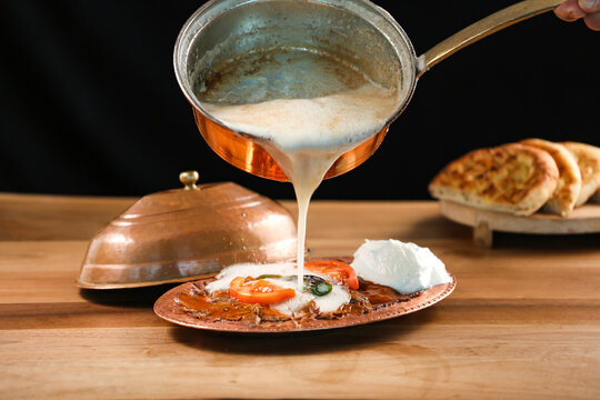 Turkish Meat Iskender Kebab topped with creamy sauce yogurt, tomato and green chilli served in golden sizzling plate with pita bread isolated on wooden table side view of traditional turkish food