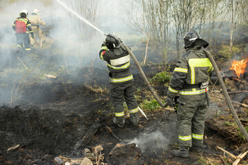 Two rescuers extinguish flames. Firefighters are fighting fire. Large hose with water pressure.