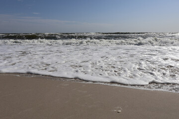 Ocean waves with white foam rolling onto a sandy beach under a clear blue sky, capturing the tranquility of the seaside.