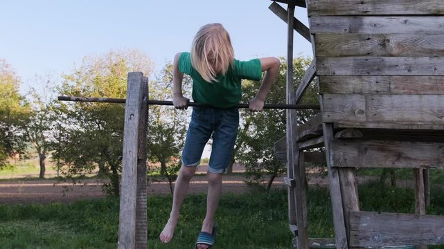 Young child swinging and hanging upside down on crossbar, showcasing playful energy in a vibrant playground setting