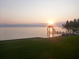 Flathead lake lodge pier jetty over the water at sunset with few clouds in the sky, grass,...