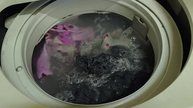Dirty clothes spinning in a top-loading washing machine. Laundry and house keeping concept