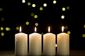 Four burning white candles on a festive black background with golden decoration, close-up shot. Advent, Christmas, holiday, and tradition concepts.