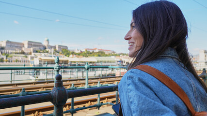 A lovely smiling woman with a backpack, enjoying seeing the city. Tourist and cities concept