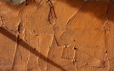 A wall with a brown texture and a shadow on it. The shadow is on the wall and it is not clear what the shadow is