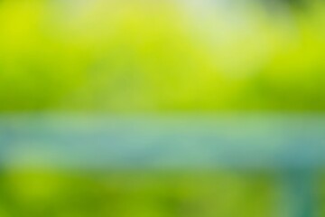 A blurry green background with a green bench in the foreground. The bench is blue and is located in...