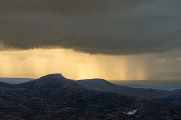 A dramatic landscape featuring heavy rain on a distant sea, illuminated by sunset rays breaking through storm clouds. Scenic view on sea