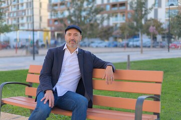 Obraz premium Man sitting on a bench in the park calm and smiling