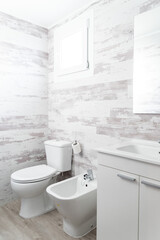 Modern bathroom with white wood-like wall tiles, featuring a white toilet, bidet, sink, and cabinet
