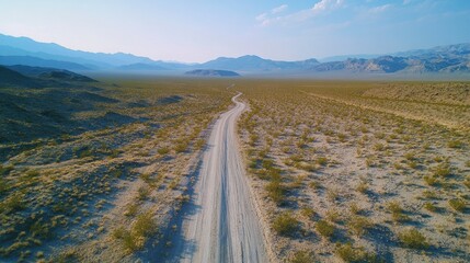 Serene Aerial View of a Winding Dirt Road Through a Desert Landscape Surrounded by Mountains and Vast Open Spaces Under a Clear Blue Sky
