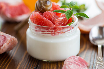 homemade sweet yogurt in a glass jar with pieces of red ripe grapefruit and honey, on a wooden table