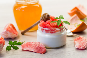 homemade sweet yogurt in a glass jar with pieces of red ripe grapefruit and honey, on a wooden table