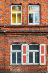 Red brick building with white window frames and open shutters during daylight hours