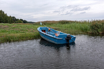 A blue fishing boat anchored quietly in a calm waterway surrounded by tall grasses during the day