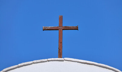 Altes christliches Kreuz aus braunem verwitterten Holz vor blauem Himmel auf einem weißen...