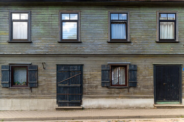 Old wooden house with rustic shutters and weathered facade in a quiet neighborhood on a sunny day