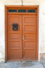 Charming wooden door painted in orange hues, featuring a mailbox and number six, located in a quaint neighborhood