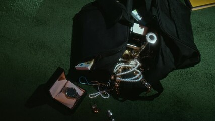 View from above of black bag of burglar with banknotes, jewellery and candlestick on floor, open case with watch next to it