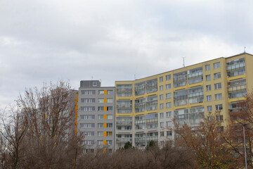 The apartment complex has a vibrant yellow and grey color scheme contrasted by a cloudy sky