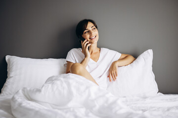 Young woman lying in her bed at home and using mobile phone