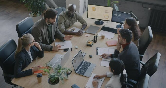 High angle view of businesspeople creative team sharing ideas talking around table in boardroom in office. Brainstorming and professional meeting in office.